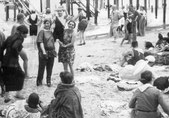 Busy beach scene with two women holding a small boy up between them.