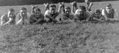Young people belly-flopped in a row on grassy field laughing .