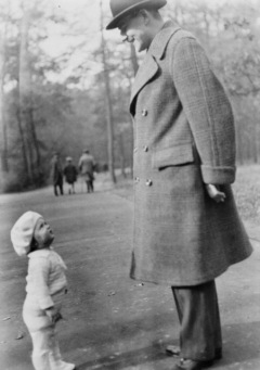 A very large man looks way down at a very small girl, both wearing winter coats and hats.