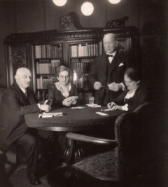 Two older couples play at cards in a library.