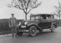 A man standing beside his enormous 1920 brougham vehicle.