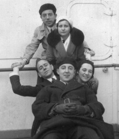 Two women and three men, all dressed warmly in suits and coats, glom onto ship chair and each other in funny pose.