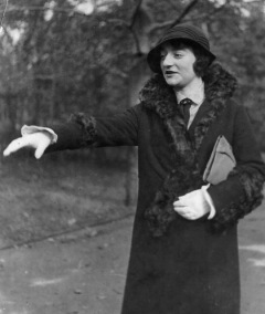 Woman in fur coat outside extends a hand toward someone out of frame.