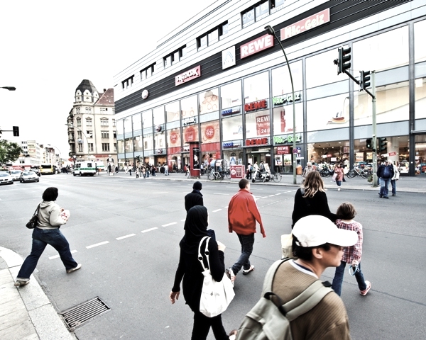 People cross street in front of modern neukolln store.